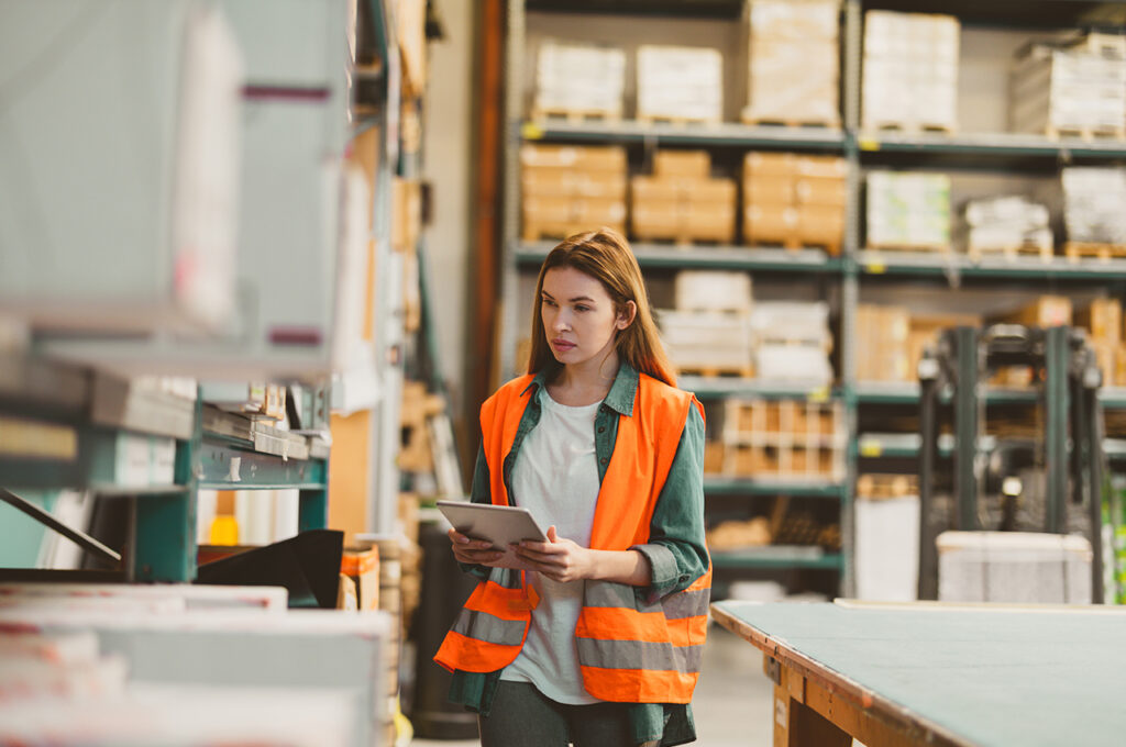 a worker with tablet in factory storehouse checking location of goods