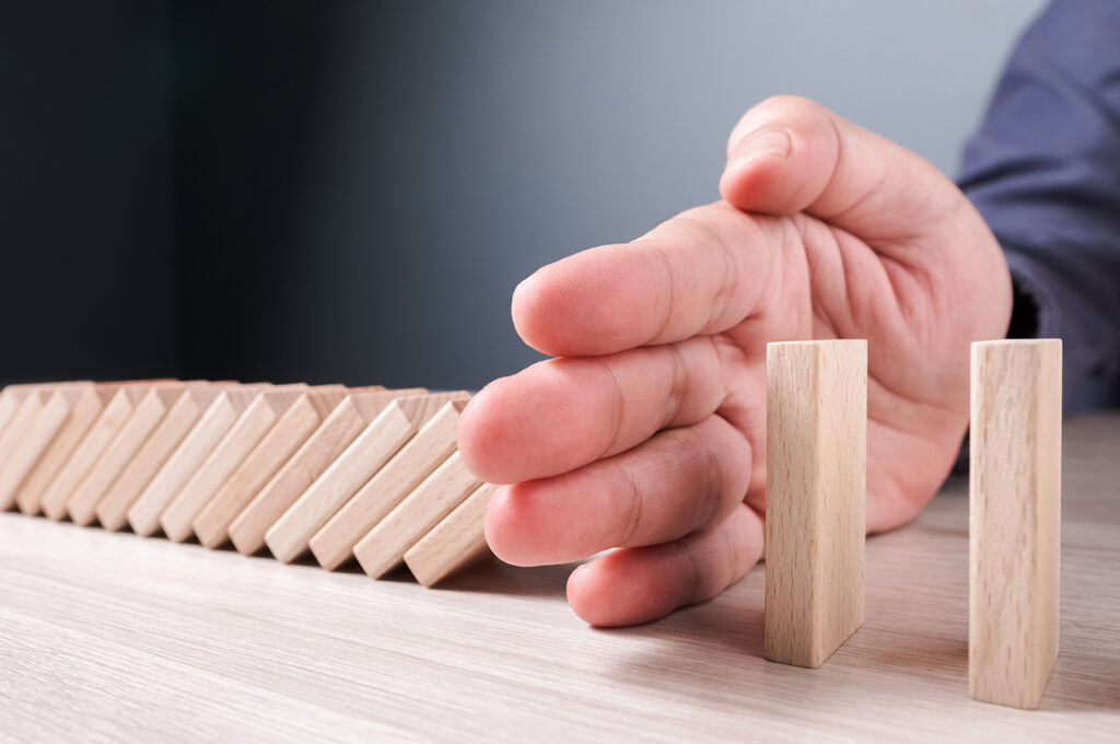 a hand blocking the trajectory of a falling line of dominoes representing supply chain disruption